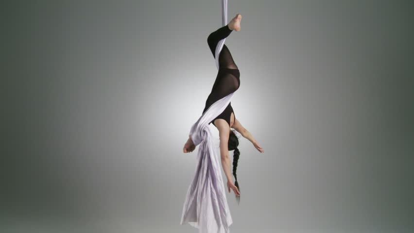 Gymnastic young woman stretches into a pose while doing aerial yoga. Wide shot