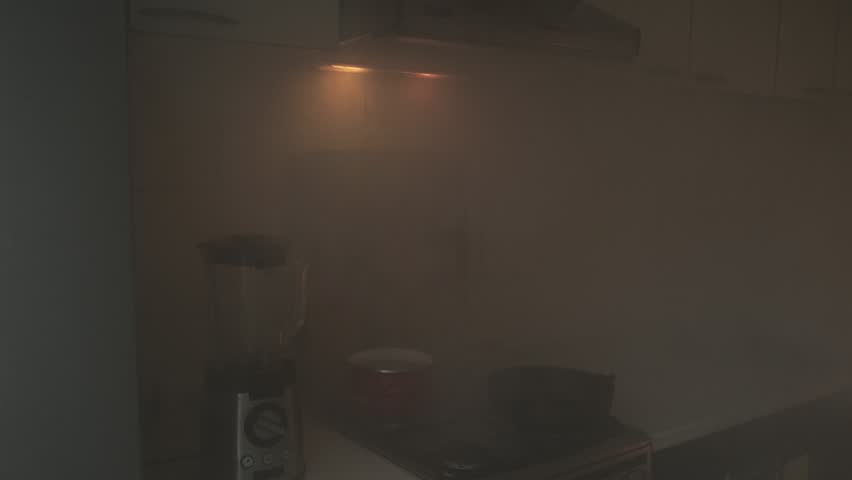 Heavy smoke engulfs a dark kitchen as flames flicker, signaling a critical fire emergency and a hazardous situation indoors
