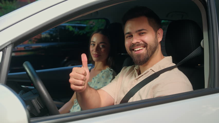 Happy Caucasian family couple sitting inside automobile man male guy driver fasten seat belt smiling showing thumb up gesture woman female girl car passenger driving safety rental service test drive