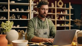 Serious Caucasian skilled man guy small business owner businessman crock potter ceramist artisan male working typing laptop networking computer online shopping ordering material inside workshop studio - Powered by Shutterstock - Get 15% off with code: PIKWIZARD15