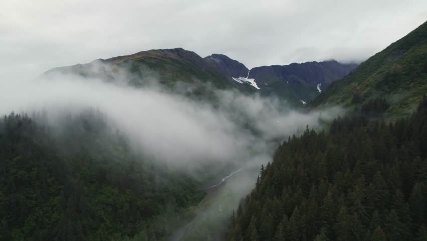 Mountainous valley with narrow river on cloudy day in Alaska, aerial view