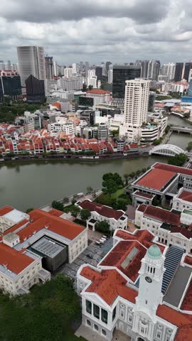 Vertical, aerial: Boat Quay during the day with cloudy sky, cityscape and Singapore River in Singapore, establishing drone shot