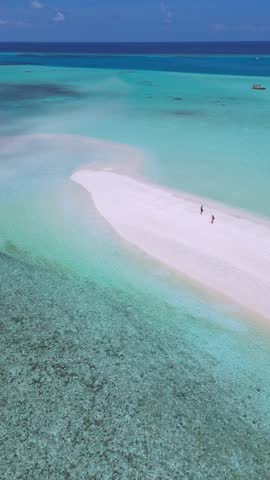 Drone shot of young tourist couple walking on white sand beach.Honeymoon romantic place on tropical sandbar while wave sea water crash on an island.Maldives