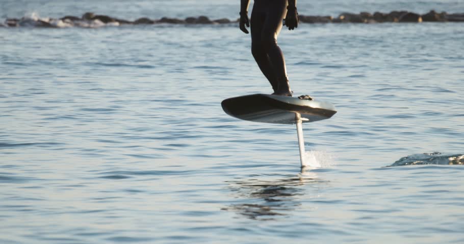 A rider balances on a hydrofoil board gliding across calm sea, with soft lighting and smooth motion captured from distance.. highlighting the joy of balance, motion, and open water