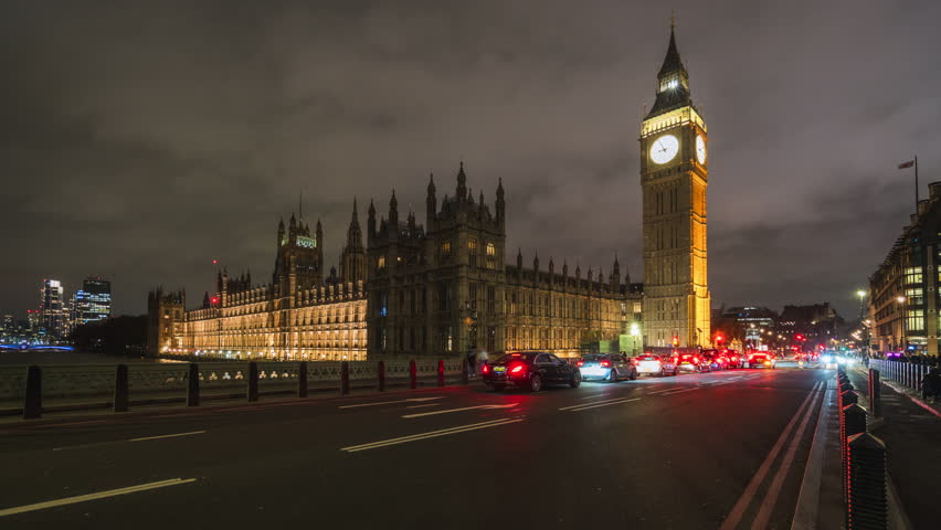 Timelapse view of traffic in front of iconic Big Ben clock tower and Palace of Westminster at night in London, UK, zooming in.