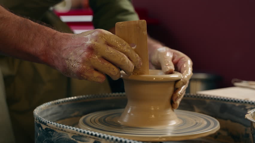Close up smiling happy focused Caucasian man guy small business owner businessman crock potter male making pottery ceramic shaping wet clay rotating wheel looking at camera wave hand indoors workshop