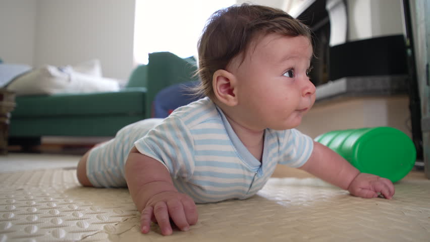Baby lying on mat, curious expression, early development, tummy time, motor skills, exploring surroundings, infant growth, learning, childhood milestone, focused gaze