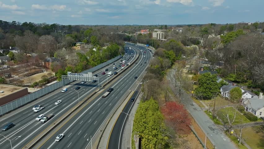 Atlanta , United States - 03 13 2025: Aerial backwards of traffic on interstate surrounded by green plants trees in spring. Parking train on railroad bridge. Suburb district of Atlanta, Georgia, USA. 