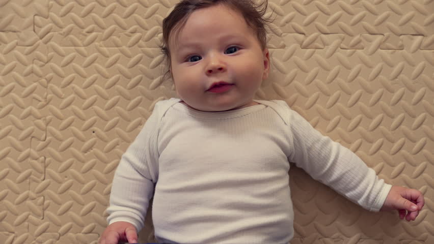 Baby lying on mat, laughing with joy, bright smile, cheerful expression, playful mood, childhood happiness, cozy home setting, relaxed and comfortable