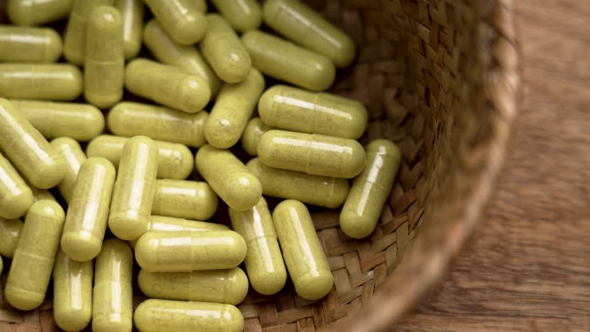 Bromelain and quercetin capsules in eco friendly wicker bowl on wooden background. Supplements filled with herbal extracts for immune health. Rotation. Top view
