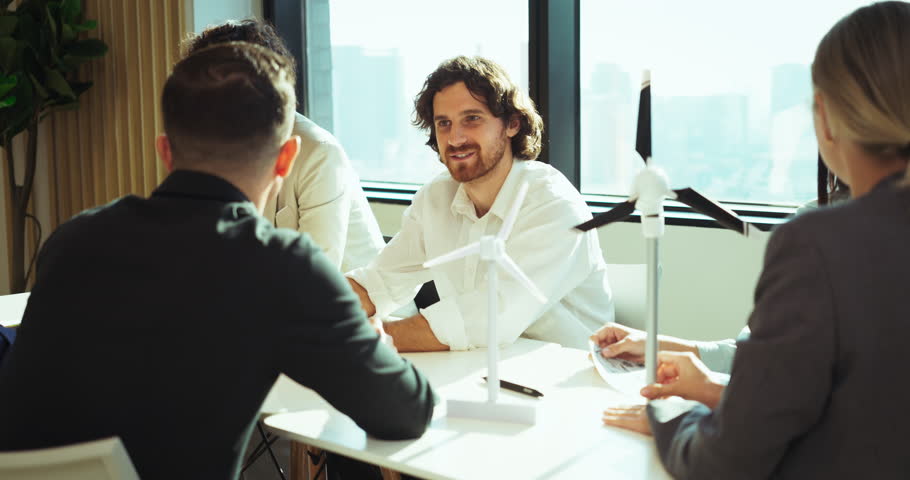 Group of professionals in a bright modern office discussing a small wind turbine model, showcasing sustainable energy concepts, teamwork, and innovation in eco-friendly project planning.