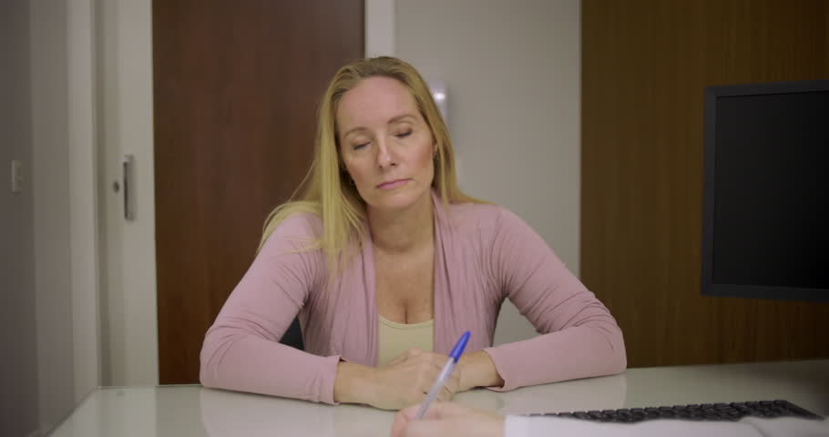 Doctor talking to middle-aged woman patient during health consultation at desk with paperwork and clipboard in private medical office