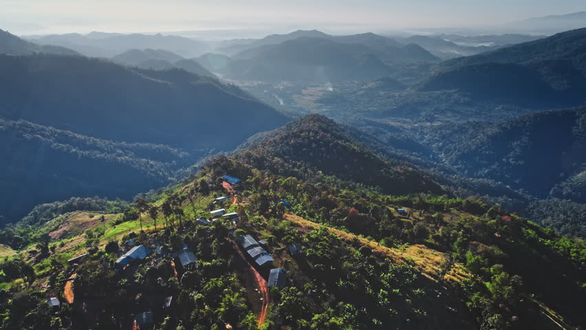 Early morning sunlight illuminating a remote mountain village in Chiang Mai Province, Thailand, reveals the tranquil beauty of lush mountains stretching into the distance