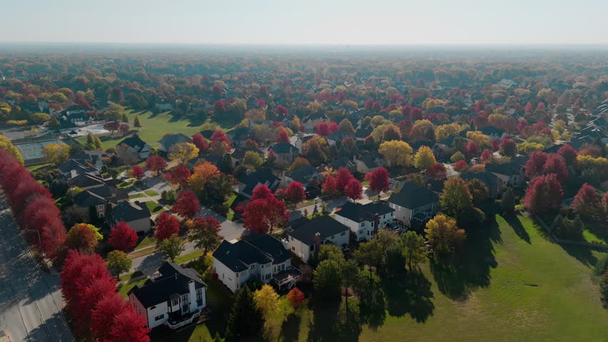 Wide view of Beaut Scenic suburban street surrounded by vibrant red and yellow autumn trees. Warm fall colors create a picturesque seasonal neighborhoods, homes, aerial view.