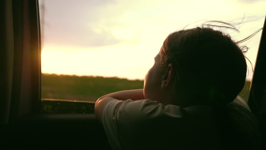 Teenager girl enjoys family trip by car. Happy family travels by car. Girl child looks out of car window. Child holiday. Family vacation. Girl kid looking out car window. Kid girl look out window sky