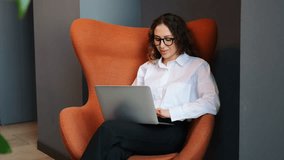 Professional Woman Working on Laptop in Stylish Orange Chair During a Modern Office Setting - Powered by Shutterstock - Get 15% off with code: PIKWIZARD15