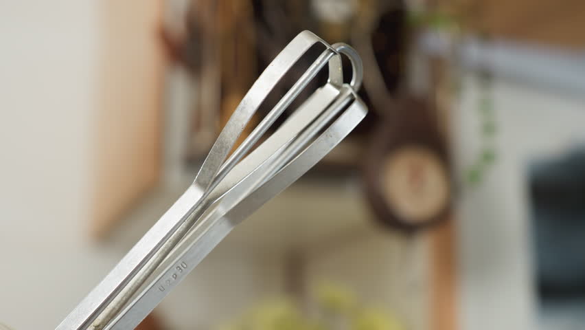 Close up of electric mixer whisk attachment rotating rapidly during mixing process in kitchen setting, showing motion blur from speed with soft background of utensils