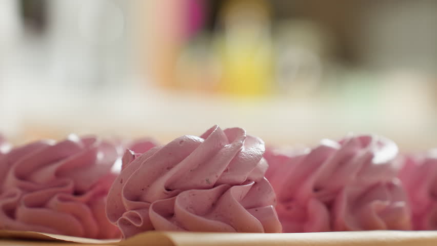 Close up of swirl pink cupcake with sugar gently sprinkled over top, sitting on parchment paper with soft blurred background, highlighting creamy texture, pastel color, and delicious dessert