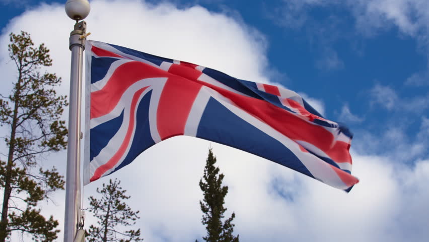 Flag of The United Kingdom of Great Britain and Northern Ireland waving in the wind against blue sky. Slow motion.