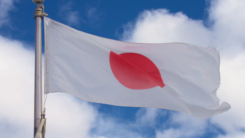 Flag of Japan waving in the wind against blue sky. Slow motion.