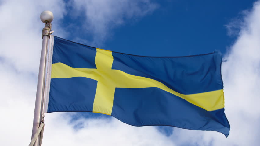 Flag of Sweden waving in the wind against blue sky. Slow motion.
