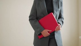 Businesswoman in gray suit holding red folder standing indoors ready for meeting or presentation with confident body language and professional attire in office or corporate environment - Powered by Shutterstock - Get 15% off with code: PIKWIZARD15