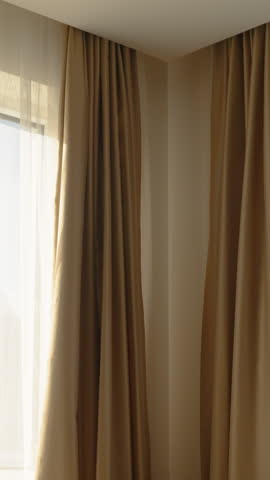 Vertical video. A brown armchair in the room beside windows through which sunlight streams. Curtains diffuse the light.