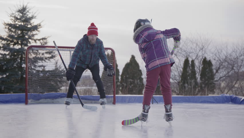 Kids playing hockey with their dad in the yard on an outdoor ice rink
