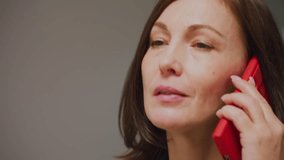 Close-up of businesswoman talking on red phone, smiling, professional woman, office environment, confident, gray suit, modern workplace, communication, business call - Powered by Shutterstock - Get 15% off with code: PIKWIZARD15