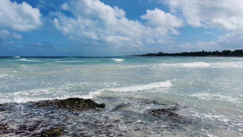 Rocky Cuban beach in Varadero, Cuba, on a cloudy day, when the sun breaks through the clouds, you can see the waves and ocean expanses. Turquoise waves. Stone slabs on the beach in the ocean. 4K	