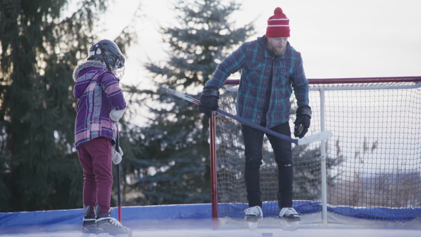 Kids playing hockey with their dad in the yard on an outdoor ice rink