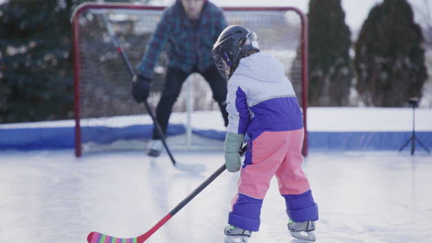 Kids playing hockey with their dad in the yard on an outdoor ice rink