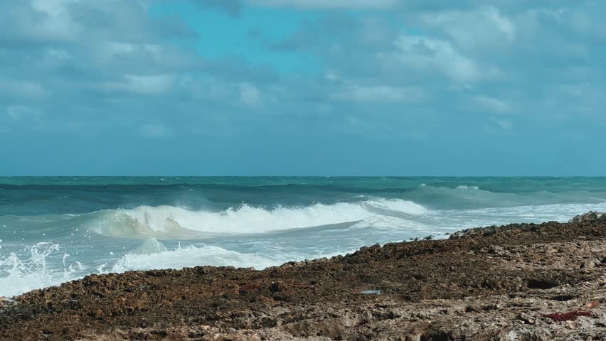 Rocky Cuban beach in Varadero, Cuba, on a cloudy day, when the sun breaks through the clouds, you can see the waves and ocean expanses. Turquoise waves. Stone slabs on the beach in the ocean. 4K	