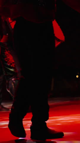 Vertical video. The stage is bathed in red light as men in Turkish costumes dance and beat drums.