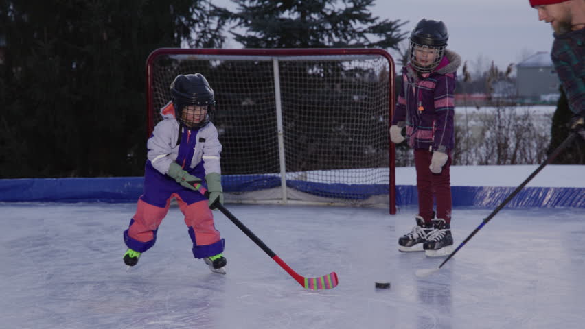 Dad spending time with daughters playing hockey on an outdoor rink