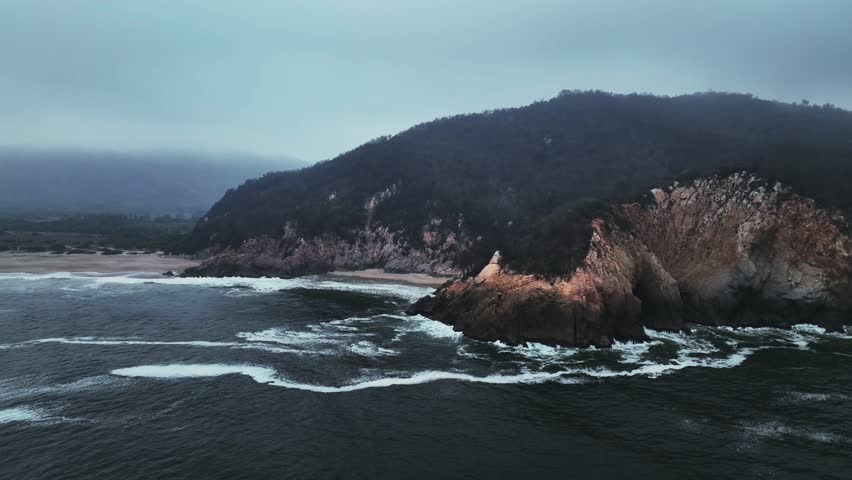 Drone view of La Peña Blanca Beach, Mexico with powerful waves crashing on rocky shore and golden sand. Manzanillo, Colima state