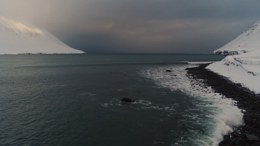 Icelandic waves breaking on snowy Arctic shores, tranquil and peaceful coastal waters with perfect waves as lone surfer paddles out