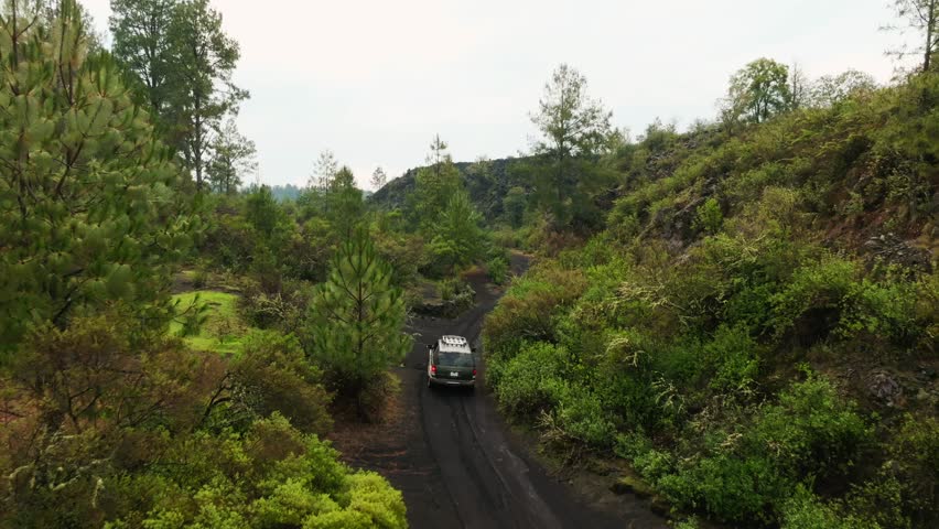 Aerial tracking shot of car on dark volcanic road sand with green scenery. Road to Paricutin Volcano, Michoacan, Mexico.