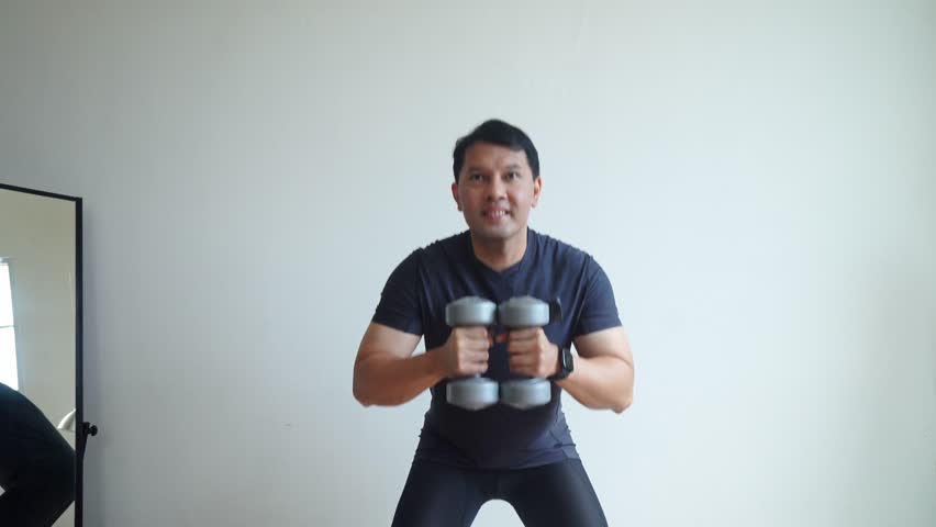 Asian Sporty Man Doing Dumbbells Workout At Home, Working On Legs Strength.