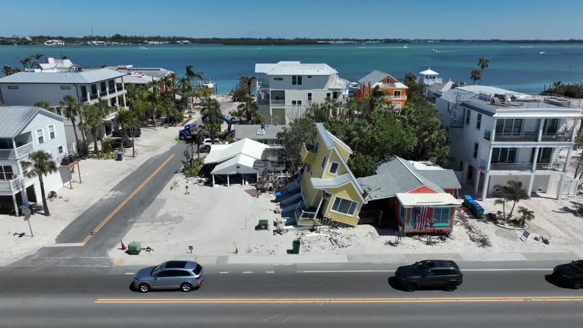 Traffic on main street of Bradenton beach in front of destroyed house after hurricane. Aerial lateral shot. Sunny day in Florida. Natural Disaster and climate change theme.
