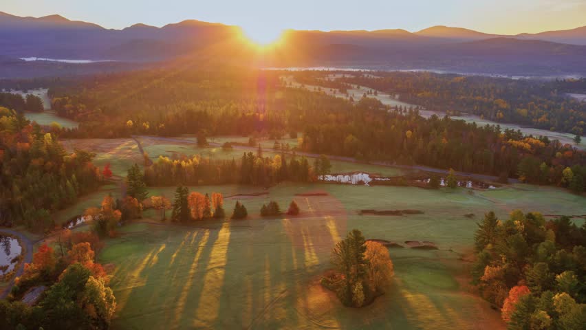A breathtaking landscape shot of the Adirondack region in New York, possibly near Lake Placid, captured during the autumn season at sunset.
