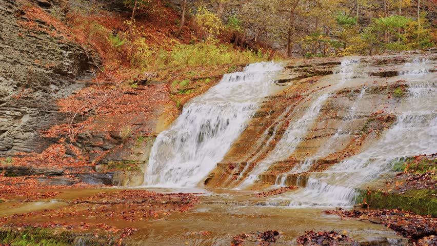 This 4K footage captures a classic fall scene in Buttermilk Falls State Park, Ithaca NY where seasonal foliage surrounds the falls with breathtaking autumn colors and calm atmosphere