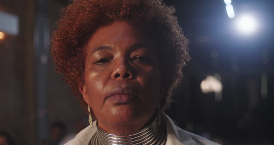 African American elderly woman with natural curly hair and statement necklace looking directly at the camera in a bold and assertive pose, indoor setting
