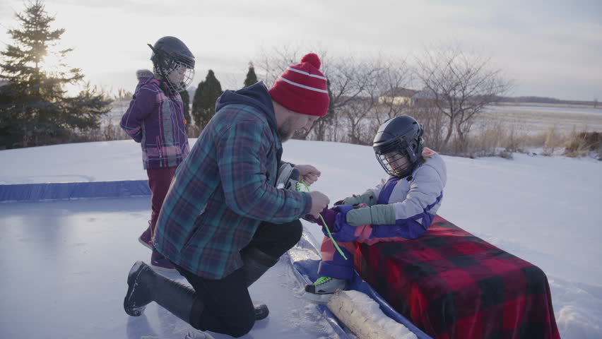 Father and daughters getting ready to play hockey on skates