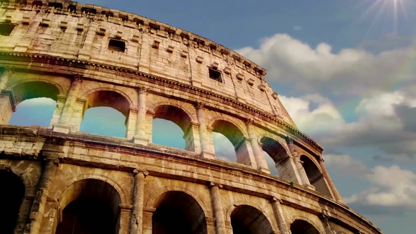 Colosseum stands proudly against vibrant blue sky with soft clouds. Sunlight illuminates ancient stone structure showcasing remarkable architecture and historical significance.