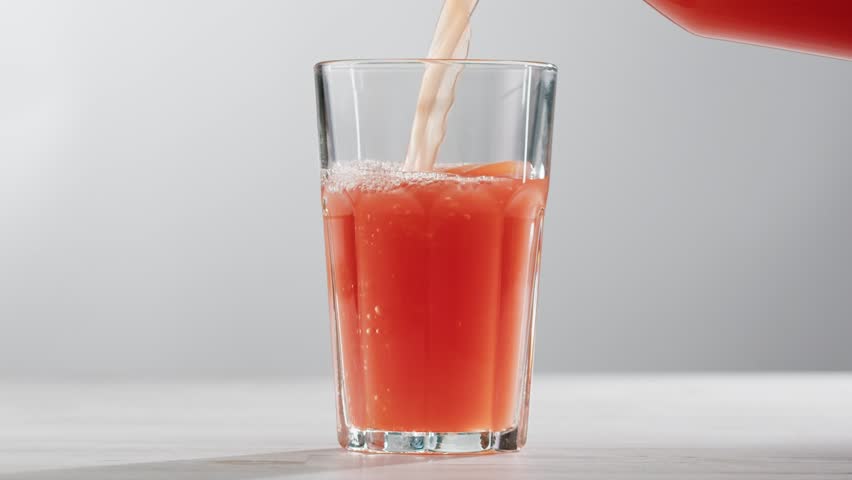 Woman pouring grapefruit juice from juicer into glass on colorful background, citrus vitamic c healthy fresh juice in cafe, morning breakfast drink.