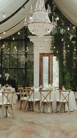 Wedding decor. This stylish venue features elegant tables, lush greenery, and beautiful chandeliers. Vertical video