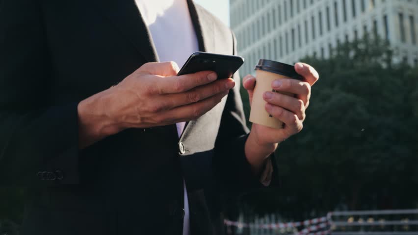 Man businessman boss making call with two phones smartphones, using applecation, walking near his office center in a dark business suit, Experienced CEO entrepreneur in modern office district