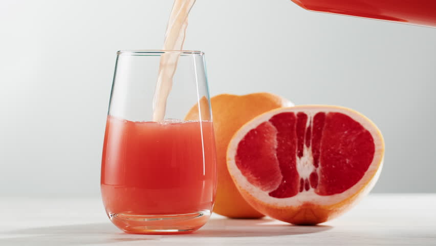 Woman pouring grapefruit juice from juicer into glass on colorful background, citrus vitamic c healthy fresh juice in cafe, morning breakfast drink.