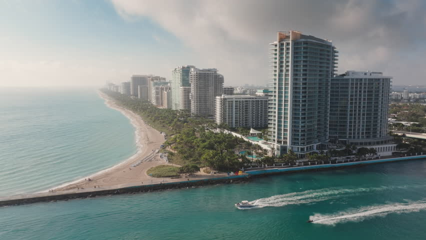 This stunning aerial shot captures the beauty of Bal Harbour Beach, Florida, with a serene sunrise, gentle waves, and modern architecture contrasting the vibrant coastal landscape